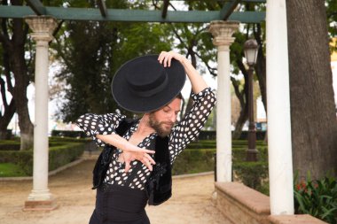 Çingene adam uzun saçlı ve sakallı flamenko dansı yapıyor mermer sütunların yanındaki parkta. Elinde siyah bir şapka tutuyor ve tutkuyla farklı duruşlar sergiliyor. Flamenko dansı.