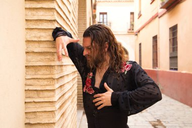 Siyah gömlek ve kırmızı güllerle flamenko dansı yapan uzun saçlı adam. Sevilla 'nın tipik dar bir sokağında elleriyle dans ediyor. Flamenko dans konsepti insanlığın kültürel mirası.