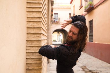 Siyah gömlek ve kırmızı güllerle flamenko dansı yapan uzun saçlı adam. Sevilla 'nın tipik dar bir sokağında elleriyle dans ediyor. Flamenko dans konsepti insanlığın kültürel mirası.