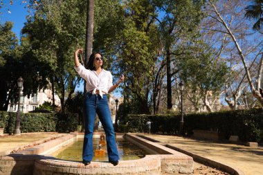 Genç, güzel, esmer bir kadın Seville 'deki bir fıskiyenin kenarında. Güney Amerikalı kadın Avrupa 'da turizm yapıyor ve tatilinin tadını çıkarıyor..