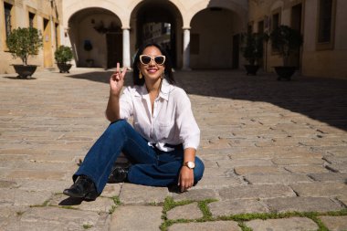 Genç, güzel, esmer, Güney Amerikalı kadın tipik bir Akdeniz şehrinde tuğla zeminde güneşleniyor. Kadın fotoğraf için poz veriyor. Tatil ve seyahat kavramı