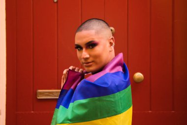 İkili olmayan, Güney Amerika kökenli ve genç biri, makyaj yapıyor ve omuzlarında eşcinsel gururu bayrağı taşıyor. Eşitlik kavramı, homoseksüellik, gay, lezbiyen, gay gururu.