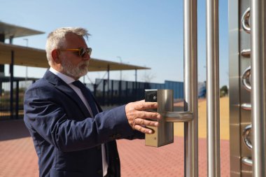 Olgun, gri saçlı, sakallı, ceketli ve kravatlı bir adam iş adamı ve yönetici olarak çalıştığı binaya giriyor. Binaya girmek için parmak iziyle kapıyı açıyor..