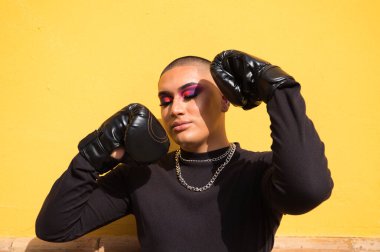 Young non-binary person wears boxing gloves on a mustard yellow background, the person is make up and does different boxing poses. Concept equality, homosexuality, gay, lesbian, gay pride. clipart