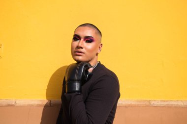 İkili oynamayan genç kişi hardal sarısı arka planda boks eldiveni giyiyor. Makyaj yapıyor ve farklı boks pozları veriyor. Eşitlik kavramı, homoseksüellik, gay, lezbiyen, gay gururu.