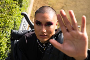 İkili olmayan ve Güney Amerikalı genç insan Avrupa 'da tatilde. Makyaj yapıyor ve siyah elbiseler giyiyor. Parkta oturmuş manken pozları veriyor. Gey güzellik ve moda konsepti.