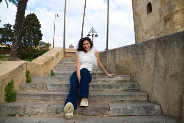 Parktaki bir merdivende oturan siyah, kıvırcık saçlı güzel bir genç kadın. Kadın farklı ifadeler kullanıyor. Kavramsal ifadeler. Gülümsüyor, üzgün, düşünüyor, eğleniyor, yaşıyor.