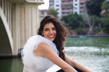 Genç, güzel, siyah, kıvırcık saçlı, şapkalı, nehir kenarında oturan bir kadın. Kadın fotoğraf için poz veriyor. Kavramsal ifadeler. Gülümse, üzül, düşün, eğlen, yaşa.