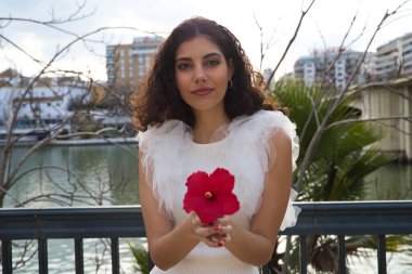 Genç, güzel, siyah, kıvırcık saçlı ve burnu kalkık bir kadın. Kadın fotoğraf için egzotik kırmızı bir çiçekle poz veriyor. Nehir arka planda görülebilir. Güzellik ve moda konsepti.