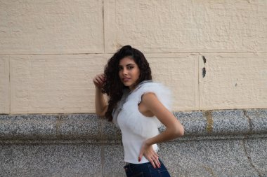 Genç, güzel, siyah, kıvırcık saçlı ve burnu kalkık bir kadın. Kadın, gri ve bej arkaplandaki fotoğraflara poz veriyor. Farklı ifadeler kullanıyor..