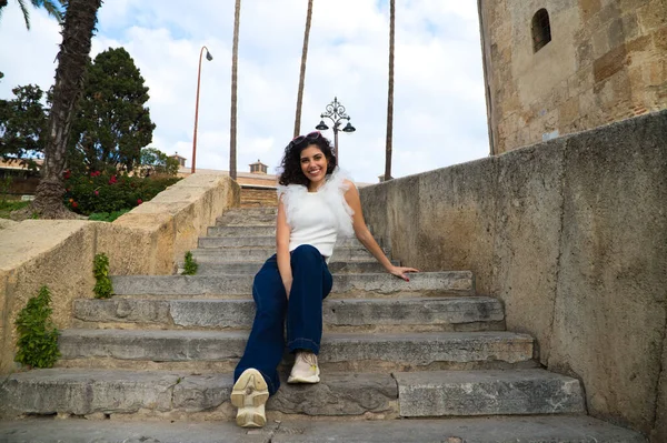 Parktaki bir merdivende oturan siyah, kıvırcık saçlı güzel bir genç kadın. Kadın farklı ifadeler kullanıyor. Kavramsal ifadeler. Gülümsüyor, üzgün, düşünüyor, eğleniyor, yaşıyor.