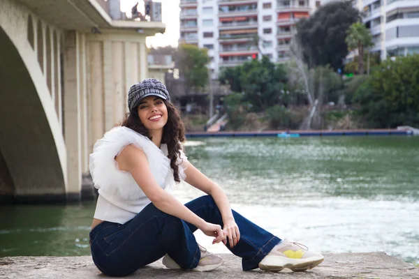 Genç, güzel, siyah, kıvırcık saçlı ve burnu kalkık bir kadın kep takıyor ve nehir kenarında oturuyor. Kadın fotoğraf için poz veriyor. Kavramsal ifadeler. Gülümse, üzül, düşün, eğlen, yaşa.