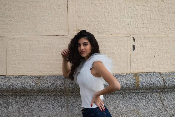 Genç, güzel, siyah, kıvırcık saçlı ve burnu kalkık bir kadın. Kadın, gri ve bej arkaplandaki fotoğraflara poz veriyor. Farklı ifadeler kullanıyor..