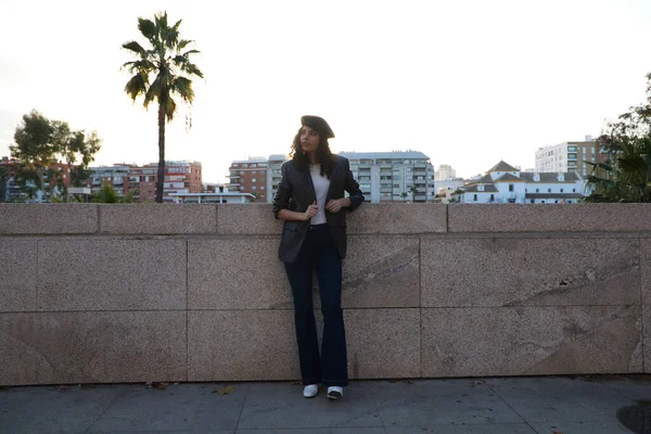 Kıvırcık kahverengi saçlı, siyah şapkalı, sıradan kıyafetler giymiş ve Sevilla 'yı gezen güzel bir genç kadının portresi. Arka planda güneş var. Turizm konsepti.