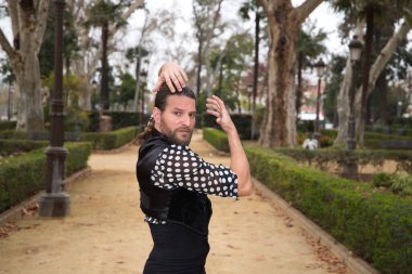 Uzun saçlı ve sakallı, flamenko dansı yapan yakışıklı orta yaşlı bir adam parkta farklı pozlar vererek tutkuyla dans ediyordu. Flamenko, dans, dans, kültür, turizm ve sanat kavramı.