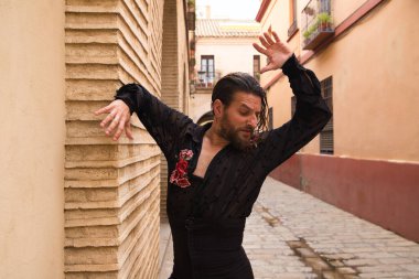 Siyah gömlek ve kırmızı güllerle flamenko dansı yapan uzun saçlı adam. Sevilla 'nın tipik dar bir sokağında elleriyle dans ediyor. Flamenko dans konsepti insanlığın kültürel mirası.