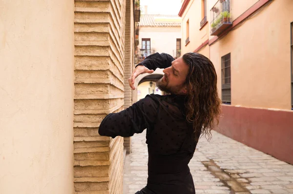 Siyah gömlek ve kırmızı güllerle flamenko dansı yapan uzun saçlı adam. Sevilla 'nın tipik dar bir sokağında elleriyle dans ediyor. Flamenko dans konsepti insanlığın kültürel mirası.