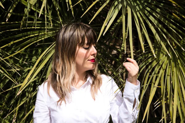 Güzel, sarışın, genç bir kadın parkta yeşil palmiye ağaçlarının önünde farklı ifadeler takınarak eğleniyor. Tatil ve boş zaman kavramı. Çeşitli ifadeler.