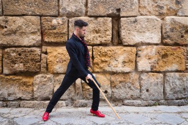 Çingene adam flamenko yapıyor, genç ve yakışıklı, siyah ayakkabılı, kırmızı ayakkabılı ve tahta sopalı, taş bir duvarın arkasında poz veriyor ve dans ediyor. İnsanlığın Flamenko kültürel mirası.