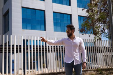 Sakallı, heykel gibi vücudu olan yakışıklı genç bir adam işaret parmağını bir yere işaret ediyor..