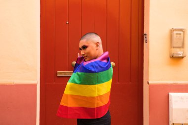 İkili olmayan, Güney Amerika kökenli ve genç biri, makyaj yapıyor ve omuzlarında eşcinsel gururu bayrağı taşıyor. Eşitlik kavramı, homoseksüellik, gay, lezbiyen, gay gururu.