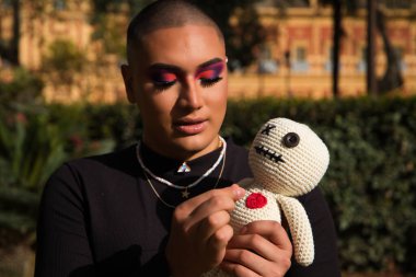 İkili olmayan ve Güney Amerika 'dan gelen genç bir insan ona iğne batıran bir bebekle vudu yapıyor. Makyaj yapıyor ve siyah elbiseler giyiyor. Kara büyü kavramı.