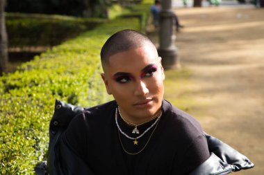 İkili olmayan ve Güney Amerikalı genç insan Avrupa 'da tatilde. Makyaj yapıyor ve siyah elbiseler giyiyor. Parkta oturmuş manken pozları veriyor. Gey güzellik ve moda konsepti.