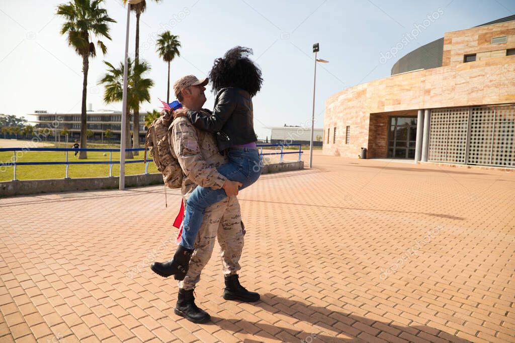 An African-American woman jumps on her soldier boyfriend who has come home from the war. They are going to melt in a loving embrace and look at each other with passion and emotion. Concept war, army.