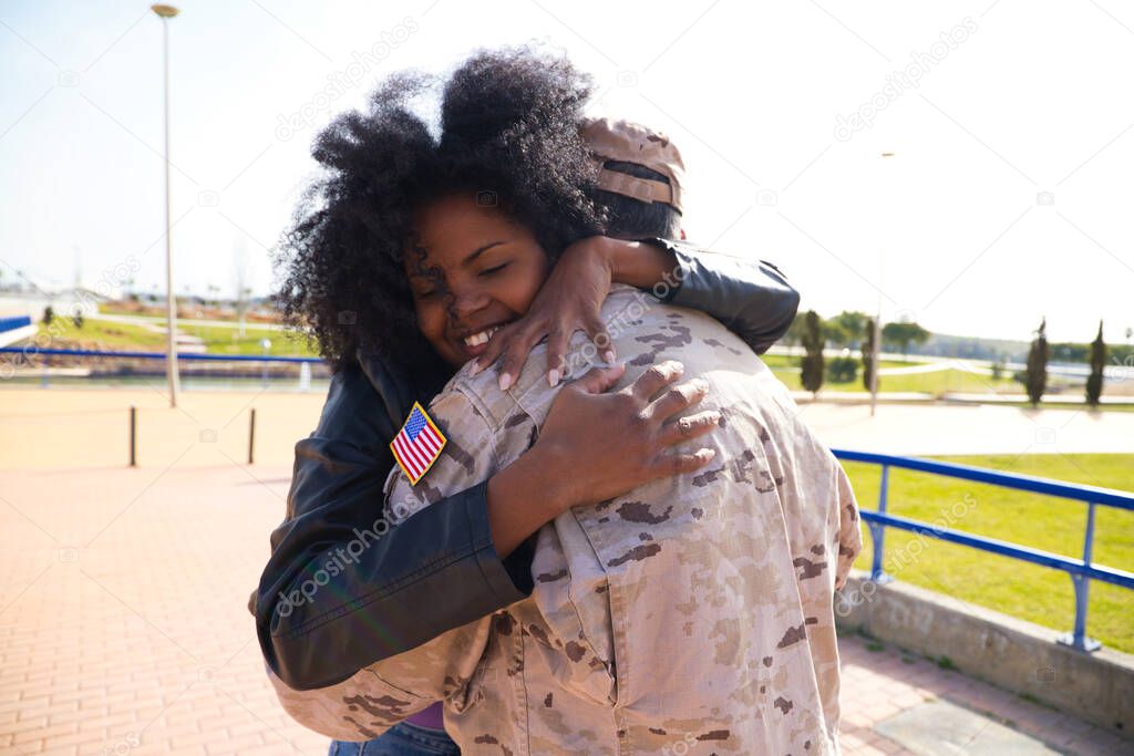 Afro-American woman and American soldier who has just arrived from the war on a peace mission embrace each other tightly. The woman is happy. Concept war and army, peace and mission.