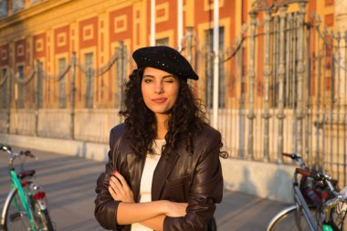 Kameraya doğru kıvırcık saçlı, siyah saçlı genç ve güzel bir kadın. O bir anıtın önünde geziyor ve arka planda bir bisiklet görebilirsiniz. Tatil ve turizm konsepti.
