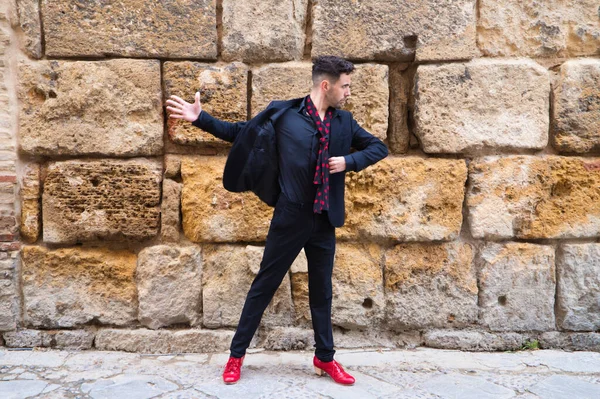 gypsy man dancing flamenco, young and handsome dressed in black and red shoes is posing and dancing on a background of a stone wall. Flamenco cultural heritage of humanity.