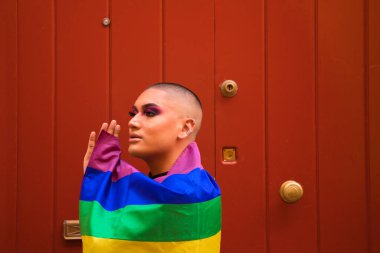 İkili olmayan, Güney Amerika kökenli ve genç biri, makyaj yapıyor ve omuzlarında eşcinsel gururu bayrağı taşıyor. Eşitlik kavramı, homoseksüellik, gay, lezbiyen, gay gururu.