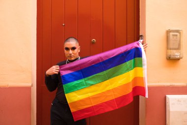 İkili olmayan, Güney Amerika kökenli ve genç, makyajlı ve kırmızı arka planda eşcinsel gurur bayrağı taşıyor. Eşitlik kavramı, homoseksüellik, gay, lezbiyen, gay gururu.