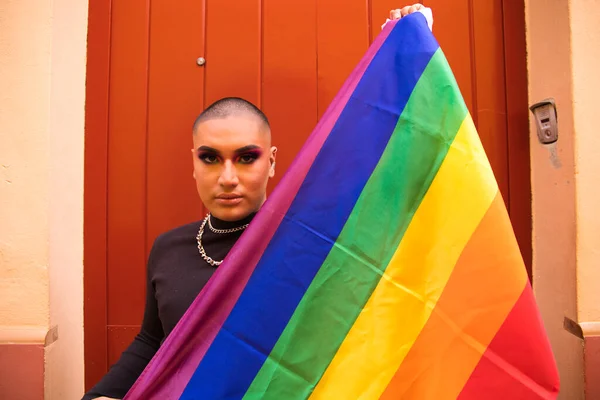 İkili olmayan, Güney Amerika kökenli ve genç, makyajlı ve kırmızı arka planda eşcinsel gurur bayrağı taşıyor. Eşitlik kavramı, homoseksüellik, gay, lezbiyen, gay gururu.