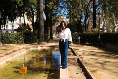 Genç, güzel, esmer bir kadın Seville 'deki bir fıskiyenin kenarında. Güney Amerikalı kadın Avrupa 'da turizm yapıyor ve tatilinin tadını çıkarıyor..