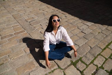 Genç, güzel, esmer, Güney Amerikalı kadın tipik bir Akdeniz şehrinde tuğla zeminde güneşleniyor. Kadın fotoğraf için poz veriyor. Tatil ve seyahat kavramı