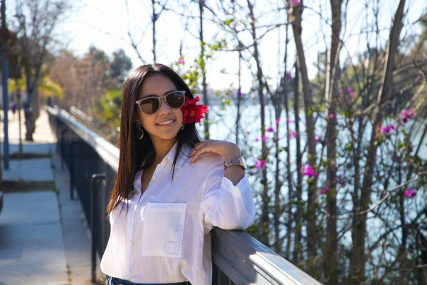 来自南美的年轻貌美的女子游览欧洲 这个女人头上戴着一朵红花 靠在塞维利亚河边的栏杆上 旅行和旅游概念 — 图库照片
