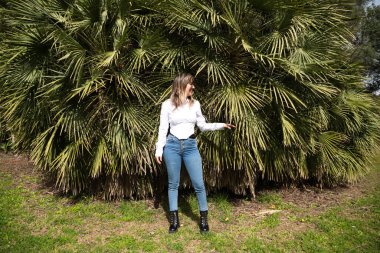 Güzel, sarışın, genç bir kadın parkta yeşil palmiye ağaçlarının önünde farklı ifadeler takınarak eğleniyor. Tatil ve boş zaman kavramı. Çeşitli ifadeler.
