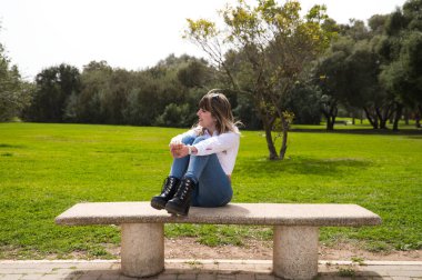 Güzel, sarışın, genç bir kadın bankta oturmuş farklı pozlar ve ifadeler veriyor. Kadın, şehirde tatilde. Seyahat ve tatil konsepti.