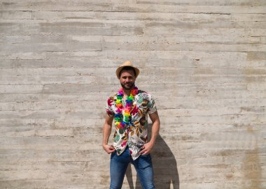 Havai çiçekli gömlek, şapka ve renkli çiçekli kolye giyen yakışıklı bir genç. Adam çok mutlu. Arka plan gri duvar. Seyahat ve tatil konsepti.