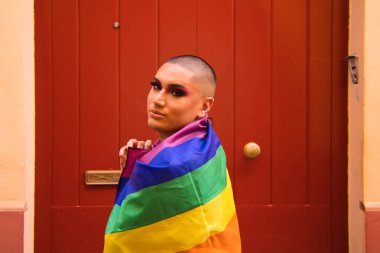 İkili olmayan, Güney Amerika kökenli ve genç biri, makyaj yapıyor ve omuzlarında eşcinsel gururu bayrağı taşıyor. Eşitlik kavramı, homoseksüellik, gay, lezbiyen, gay gururu.