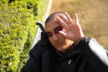 İkili olmayan ve Güney Amerikalı genç insan Avrupa 'da tatilde. Makyaj yapıyor ve siyah elbiseler giyiyor. Parkta oturmuş manken pozları veriyor. Gey güzellik ve moda konsepti.