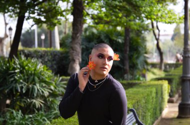 Güney Amerikalı olmayan biri saçına çiçekler takıyor, siyah elbiseler ve makyaj yapıyor. Homoseksüellik, moda ve güzellik kavramı.