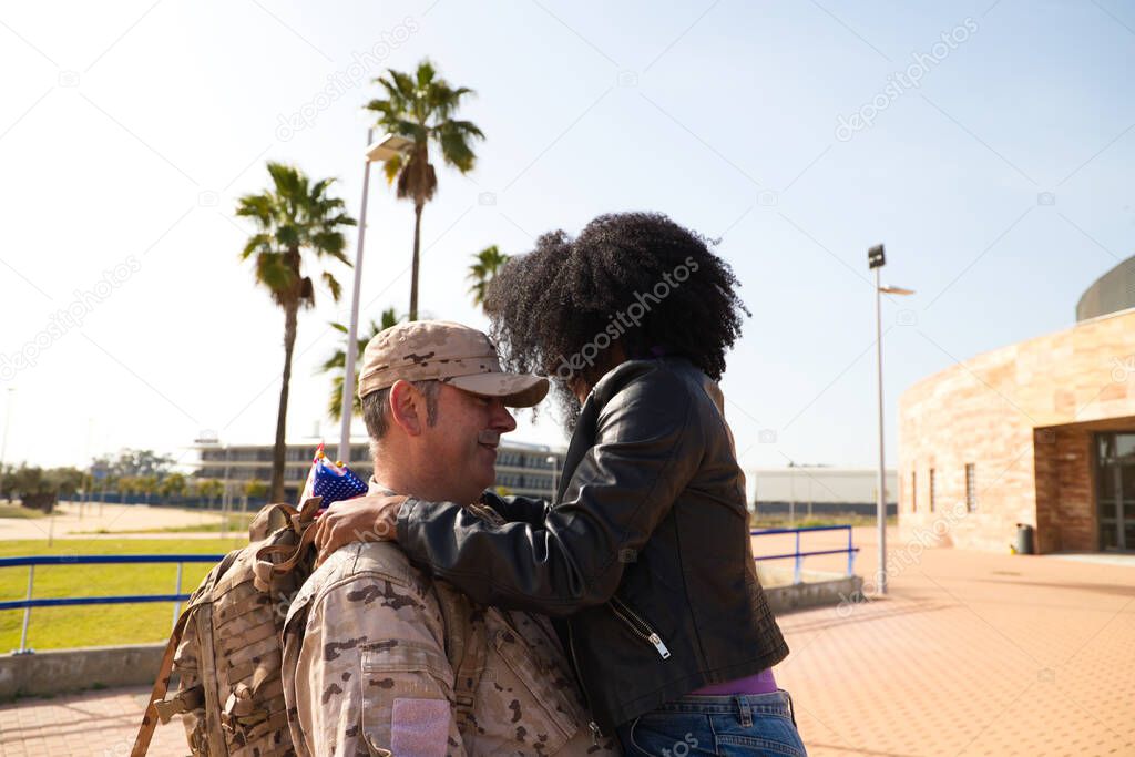 An African-American woman jumps on her soldier boyfriend who has come home from the war. They are going to melt in a loving embrace and look at each other with passion and emotion. Concept war, army.