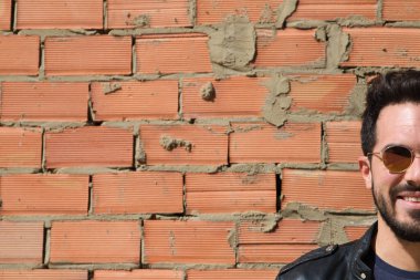 Kırmızı tuğlalı arka planda sakallı bir adamın yakın plan portresi..