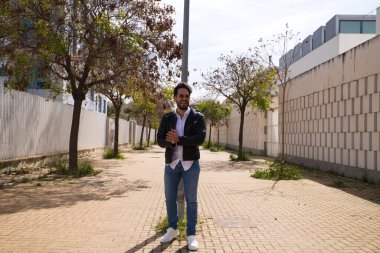 Orta yaşlı, yakışıklı ve esmer, sakallı ve vücudu yontulmuş bir adam. Siyah deri ceketli, aynalı güneş gözlüklü ve kot pantolonlu bir adam. Adam fotoğraf için poz veriyor. Erkek moda konsepti.