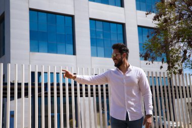 Sakallı, heykel gibi vücudu olan yakışıklı genç bir adam işaret parmağını bir yere işaret ediyor..