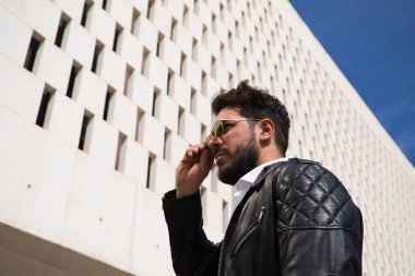 Sakallı, heykel gibi vücudu olan yakışıklı genç adam sokakta yürürken güneş gözlüğünü çıkarıyor ya da takıyor. Turizm ve şehir yürüyüşleri kavramı