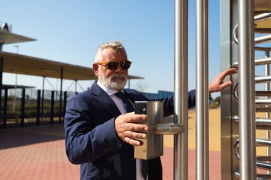 Olgun, gri saçlı, sakallı, ceketli ve kravatlı bir adam iş adamı ve yönetici olarak çalıştığı binaya giriyor. Binaya girmek için parmak iziyle kapıyı açıyor..