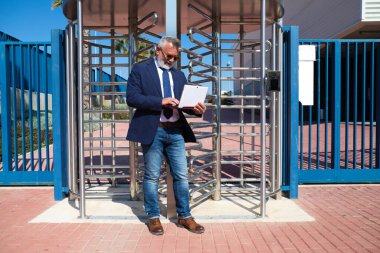 Yetişkin erkek yönetici, gri saçlı, sakallı, güneş gözlüklü, ceketli ve kravatlı sokakta dizüstü bilgisayarına danışıyor. Kavramsal işadamı ve yönetici.